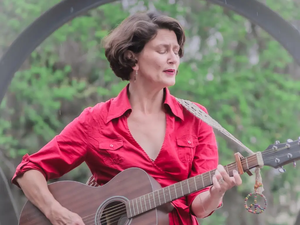Brandi Olenyik playing guitar outside with rose bushes
